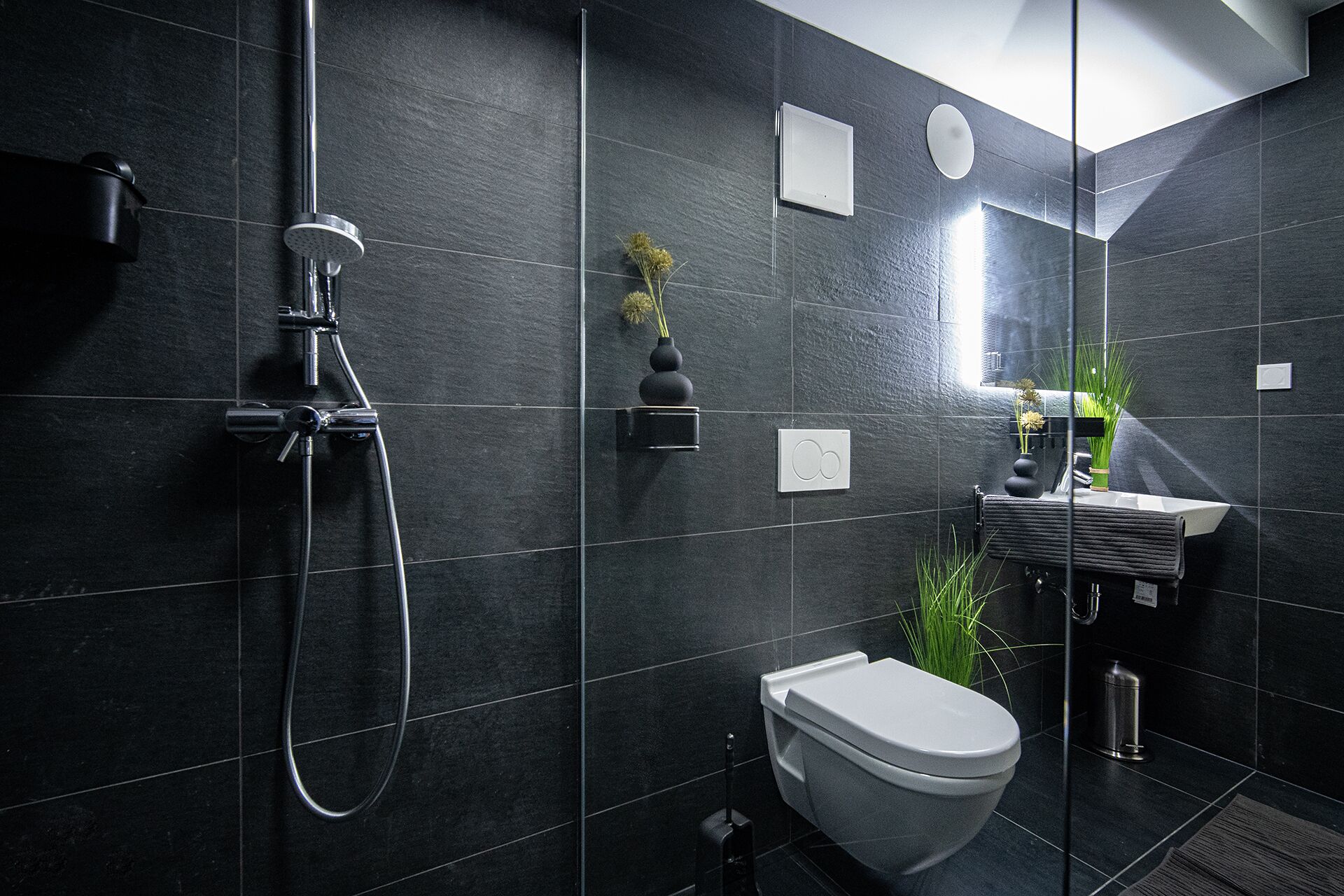 A modern bathroom with dark tiles, a shower, a toilet, and a sink with a towel rack.
