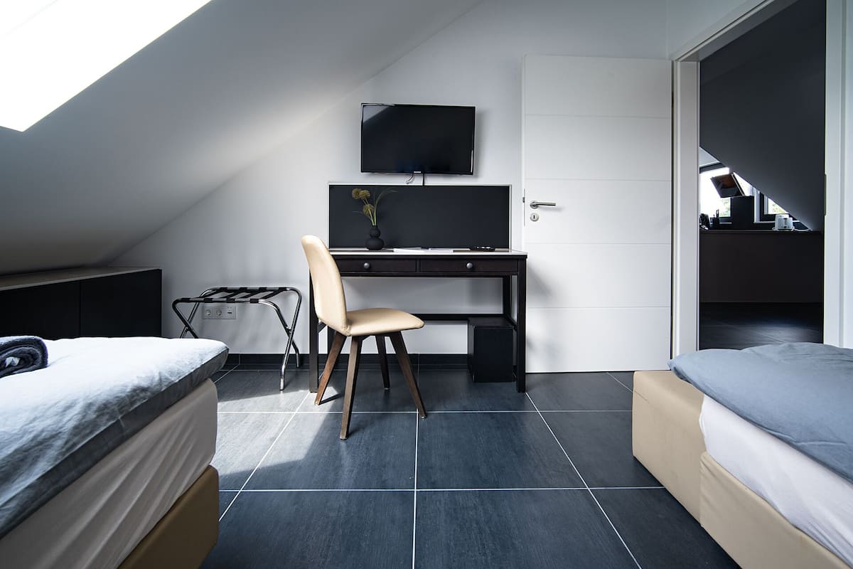 Een kleine kamer met een bed, een bureau met stoel, een televisie en een deur naar een andere kamer.