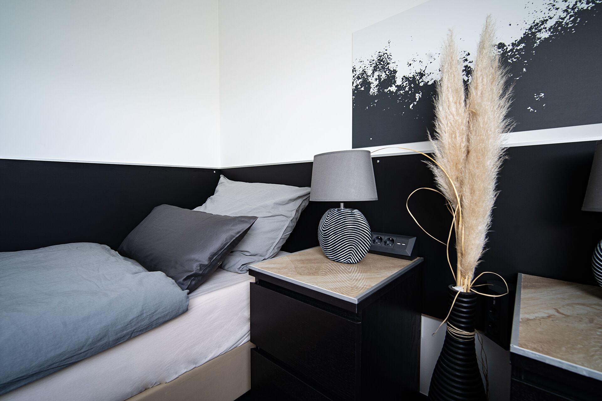 A modern bedroom with a bed, bedside table, lamp, and wall art.