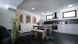 A modern kitchen with a dining area, featuring a central island, a built-in oven, and a large window. - Blauer Stein - Echo bl7a-haus (Pulheim)