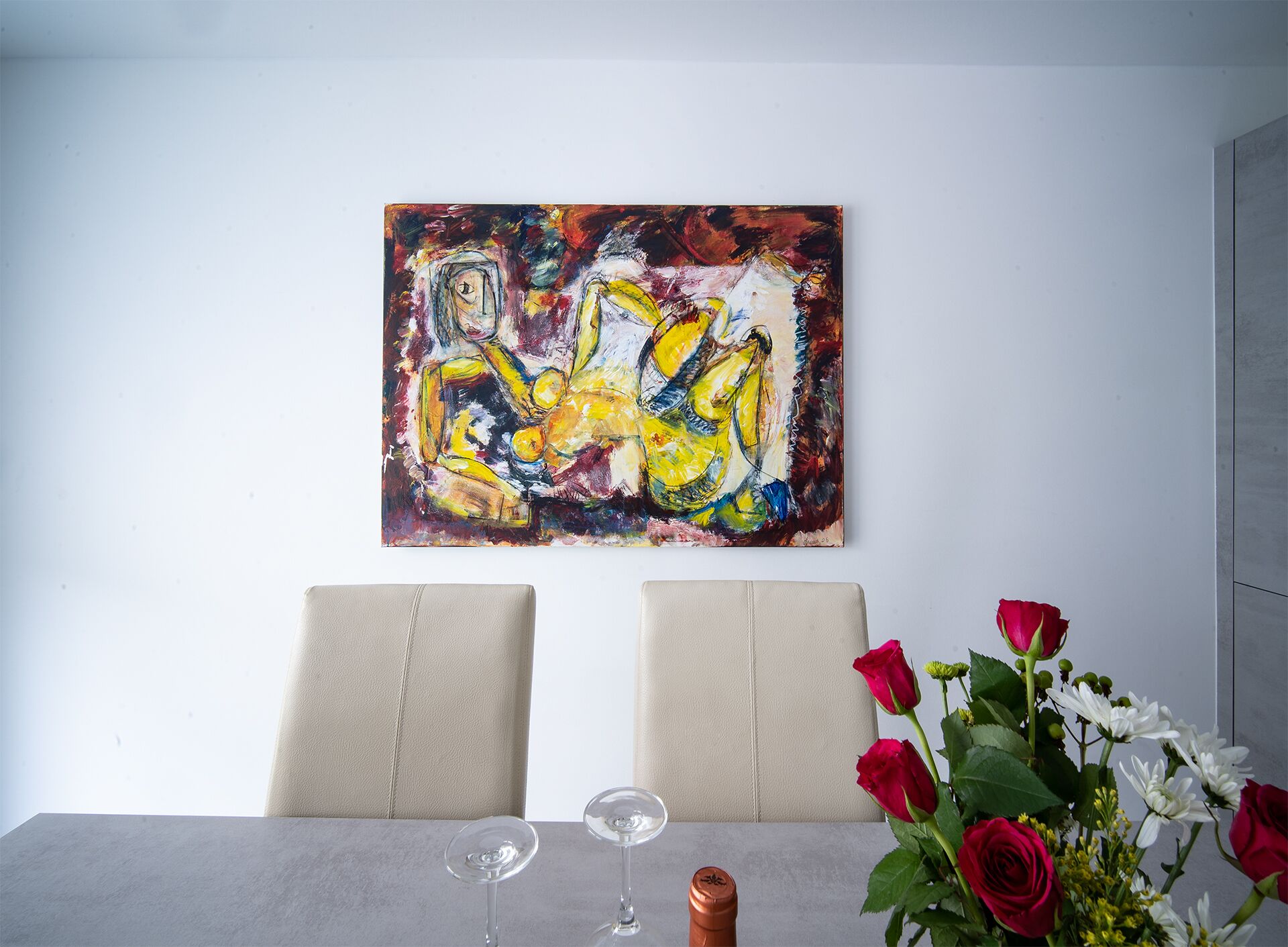 A dining table with two chairs, a vase with red and white flowers, and a painting on the wall.