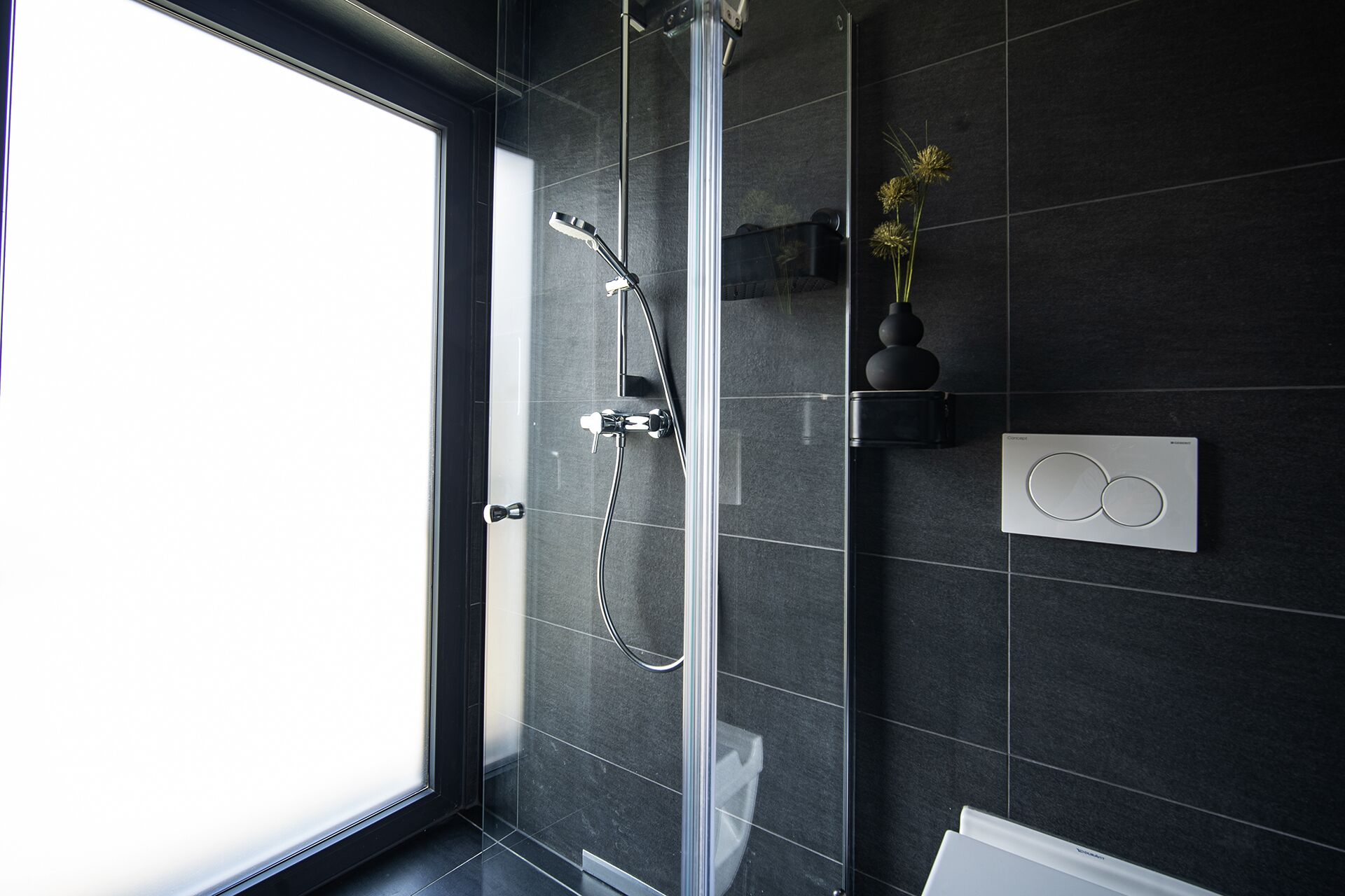 A modern bathroom with a glass shower enclosure, a toilet paper holder, and a thermostat on the wall.