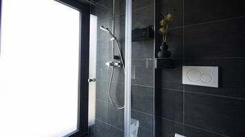A modern bathroom with a glass shower enclosure, a toilet paper holder, and a thermostat on the wall.