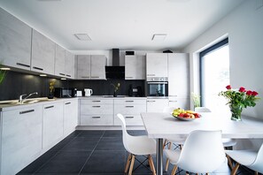 Une cuisine moderne avec des meubles blancs, un coin repas doté d’une table et de chaises blanches, et une grande fenêtre.