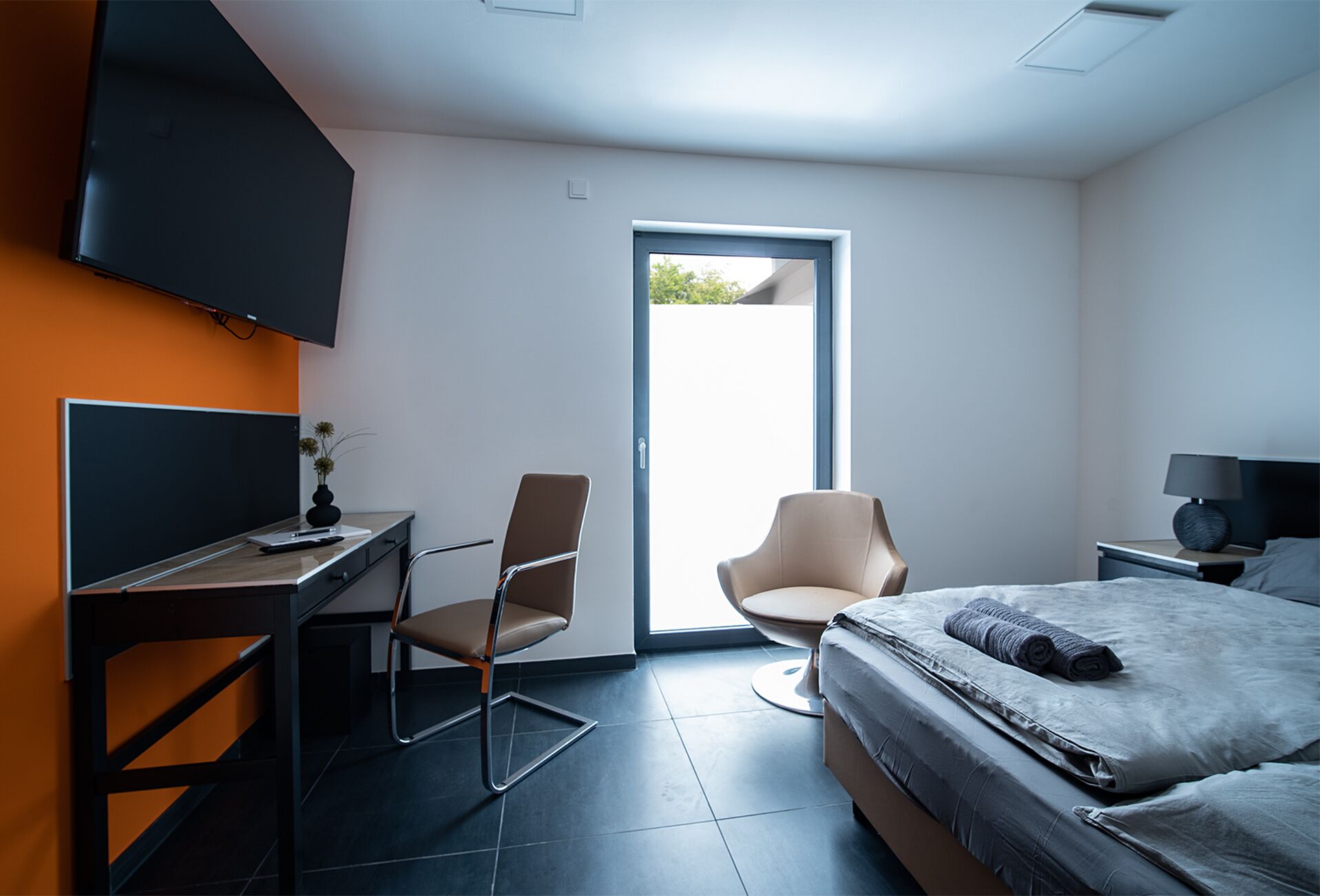 Ein modernes Hotelzimmer mit Schreibtisch, Stuhl, Bett und Fernseher.