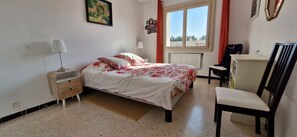 A bedroom with a bed, a chair, a desk, a radiator, and a window. - LE FLOREAL Apartment 75 m² - 2 Bedrooms - Sleeps 4 (Bandol)