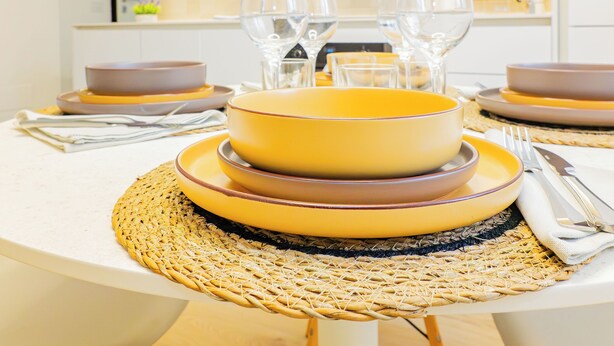 A dining table set with yellow and brown plates, clear glasses, and silverware. - Riva Real Estate - Lake Central Suite (Lecco)