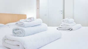 A hotel room with neatly stacked white towels on the bed and a wooden headboard. - Riva Real Estate - Lake Central Suite (Lecco)