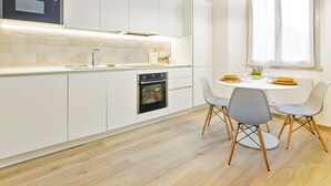 A modern kitchen with white cabinetry, a built-in oven, and a dining area with a round table and two chairs. - Riva Real Estate - Lake Central Suite (Lecco)