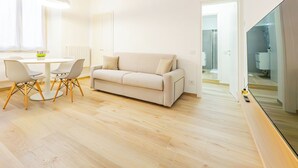 A modern living room with a beige sofa, a round dining table with chairs, and a large mirror. - Riva Real Estate - Lake Central Suite (Lecco)