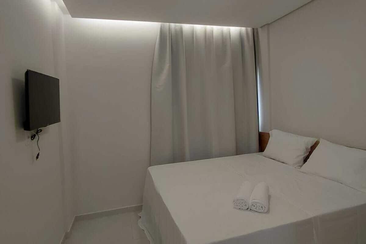 A modern hotel room with a neatly made bed, a flat-screen TV mounted on the wall, and a ceiling light.