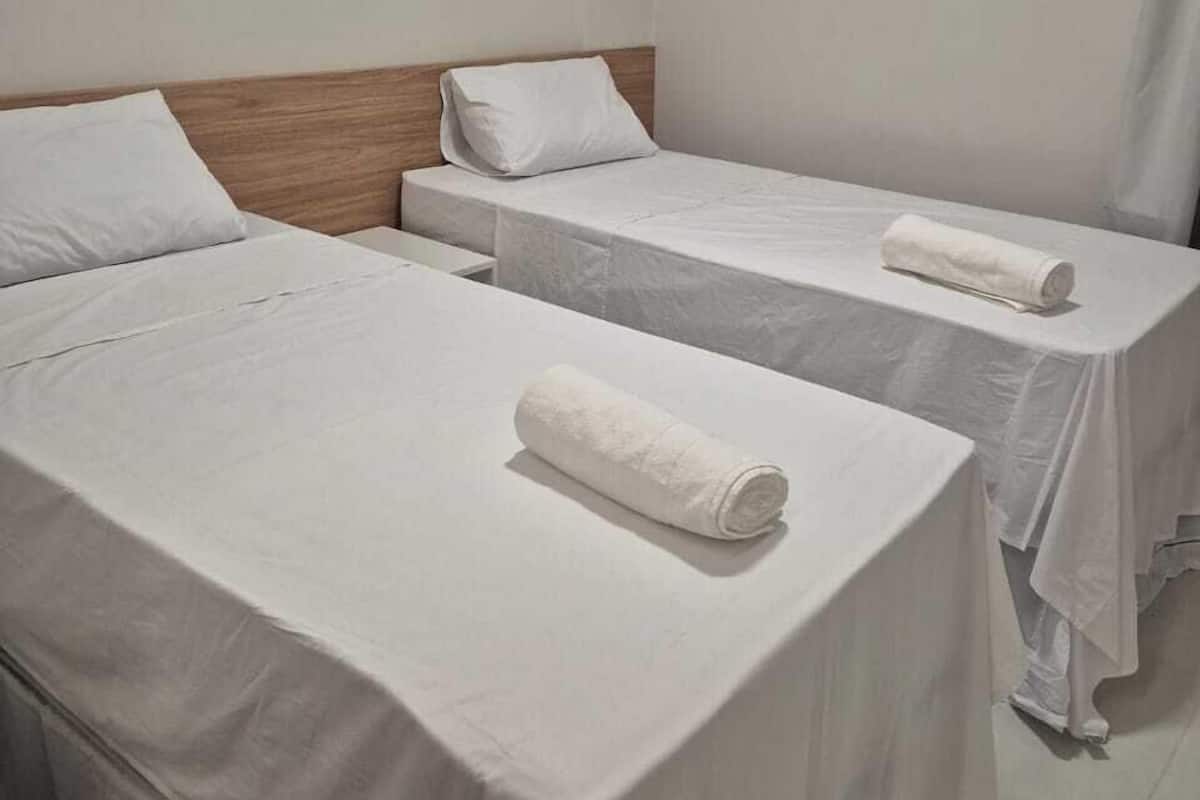 A hotel room with two single beds, each with a white bedspread and a rolled white towel on the bed.