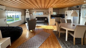 Interior acogedor de una cabaña con techo de madera, un sofá, una mesa de comedor y una zona de cocina.