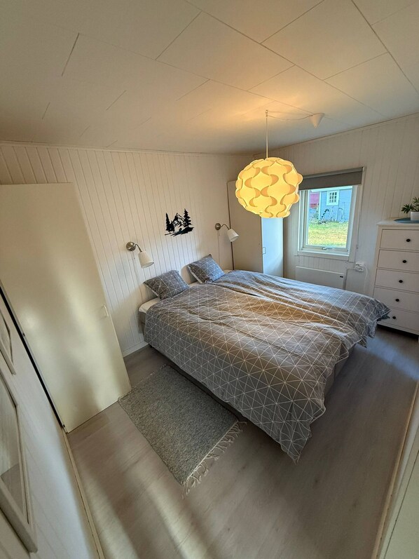 A bedroom with two beds, a window with a view of the outside, a hanging light fixture, and a dresser. - Camp Caroli Olala House (Jukkasjarvi)