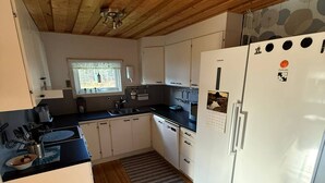 Una cocina compacta con vigas de madera en el techo, armarios blancos, un refrigerador y una ventana con vistas.