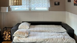 Un dormitorio con techo de madera, cama con colcha estampada, ventana con vistas y una lámpara fijada a la pared.