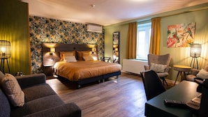 A hotel room with a large bed, a sofa, a chair, a small table, and a painting on the wall. - Hotel Brasserie de Klok (Zutendaal)
