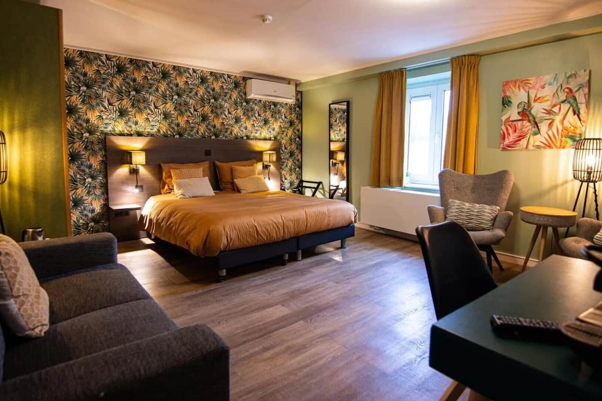 Une chambre d’hôtel avec un grand lit, un canapé, un fauteuil, une petite table et un tableau au mur.