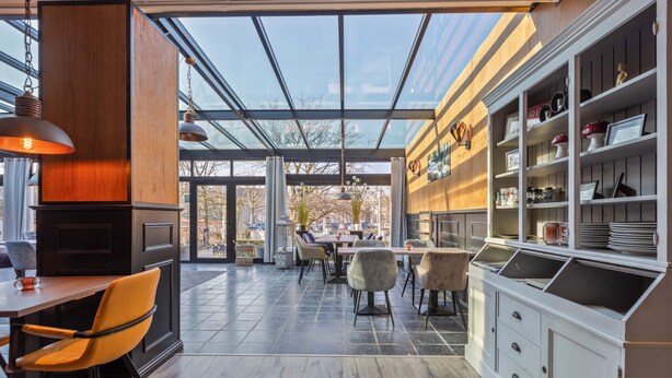 A modern kitchen with a glass ceiling, wooden cabinets, and a dining area with chairs and tables. - Hotel Brasserie de Klok (Zutendaal)
