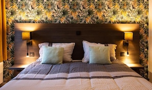 A bed with a patterned headboard, two wall-mounted lamps, and a textured bedspread. - Hotel Brasserie de Klok (Zutendaal)