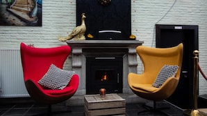 Two armchairs with patterned cushions, a fireplace, and a decorative peacock statue. - Hotel Brasserie de Klok (Zutendaal)
