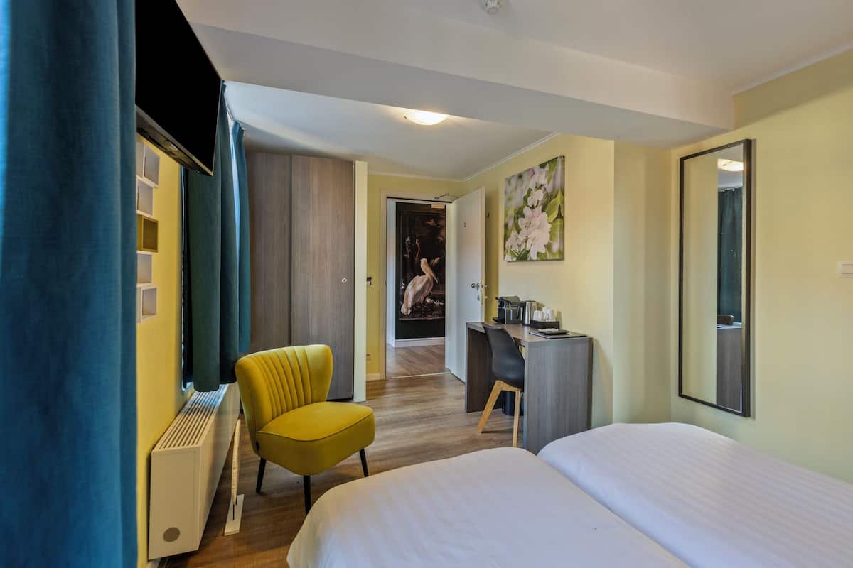 Une chambre d’hôtel avec un lit, un bureau, une chaise et un grand miroir.
