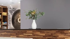 Un área de recepción con un mostrador de madera, un jarrón blanco con flores y un mural grande en la pared.