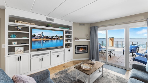 Uma sala de estar com televisão, lareira e varanda com vista.