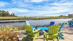 Um alpendre à beira-mar com cadeiras Adirondack e uma mesa, com vista para águas calmas e uma área gramada.