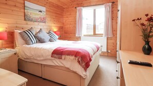 Ein Schlafzimmer einer Holzhütte mit einem Bett, Nachttischlampen, einem Fenster mit Vorhängen und einem Bild an der Wand.