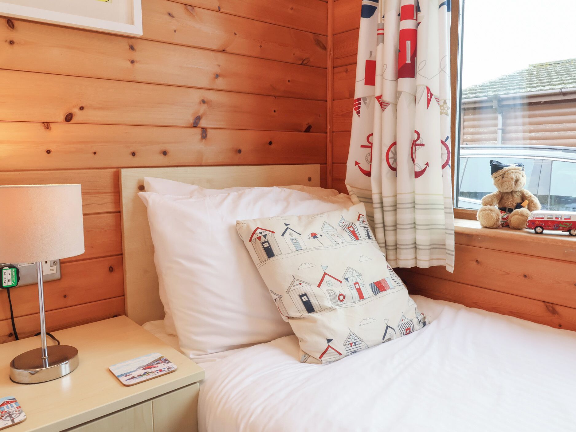 Une chambre rustique en bois avec un lit, une table de chevet, une lampe, un ours en peluche et une voiture jouet près de la fenêtre.
