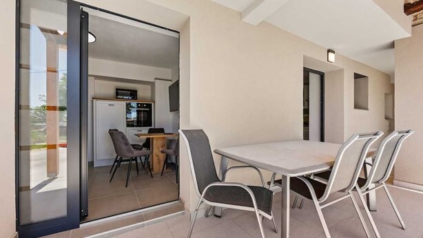 A modern dining area with a glass door leading to a kitchen, metal chairs, and a light-colored table. - Holiday Apartment Toronda (Vrvari-Poreč)