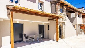 En overdækket terrasse med et bord og stole, en træpergola og en stensokkel til skorsten.