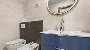 A modern bathroom with a bidet, a toilet, and a sink with a mirror above. - Holiday Apartment Vanga (Vrvari-Poreč)