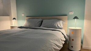 A neatly made bed with a grey comforter and pillows, two bedside tables with lamps, and a wall-mounted thermostat. - B&B Malnati 3 Urban Living Milanosansiro (Milan)