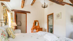 A bedroom with a large bed, a wooden dresser, a mirror, and a chandelier. - Farmhouse Cottage (Keswick)
