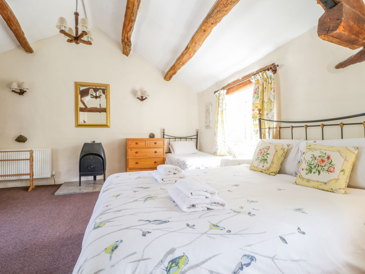A bedroom with a large bed, two bedside tables, a dresser, a radiator, and a ceiling with exposed wooden beams.