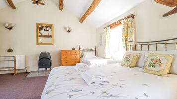 A bedroom with a large bed, two bedside tables, a dresser, a radiator, and a ceiling with exposed wooden beams.