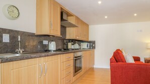 A modern kitchen with wooden cabinets, a stainless steel sink, and a red sofa in the living area. - Farmhouse Cottage (Keswick)