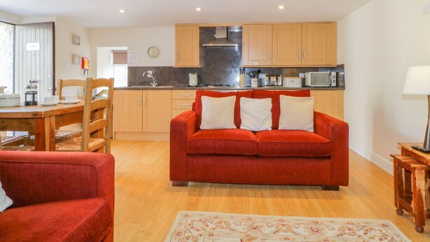 A compact living space with a kitchen area, a dining table, and a red sofa. - Farmhouse Cottage (Keswick)