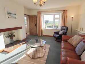 A living room with a leather sofa, a glass coffee table, a wooden door, and a large window with curtains. - 2 Lupton Hall Cottages (Carnforth)