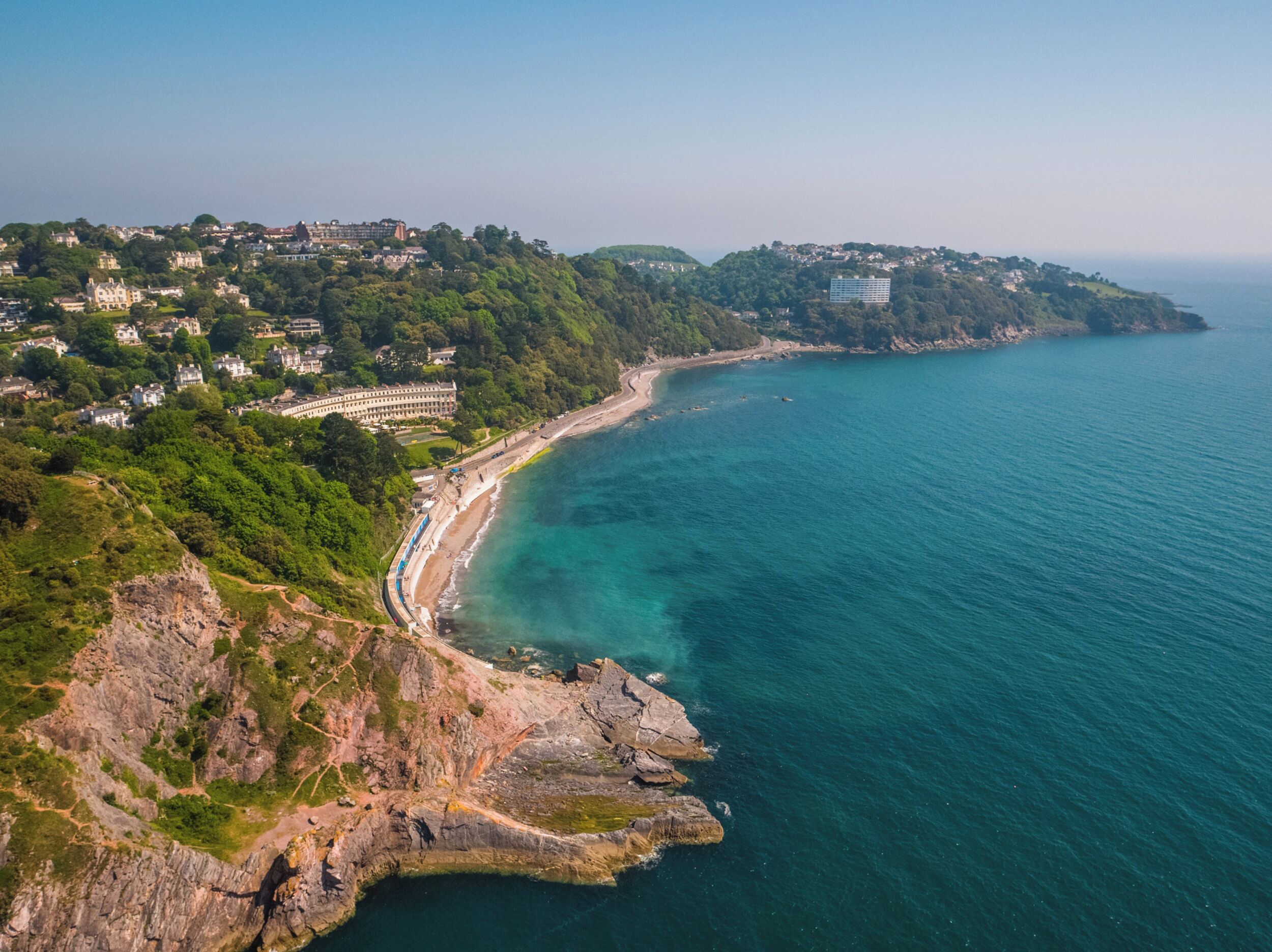 An aerial view of a coastal area with a beach, rocky coastline, and residential buildings.