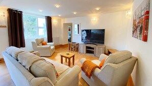 A modern living room with a large sofa set, a television, and a coffee table. - Lower Stable - The Stables Apartments at Meadfoot Bay (Torquay)