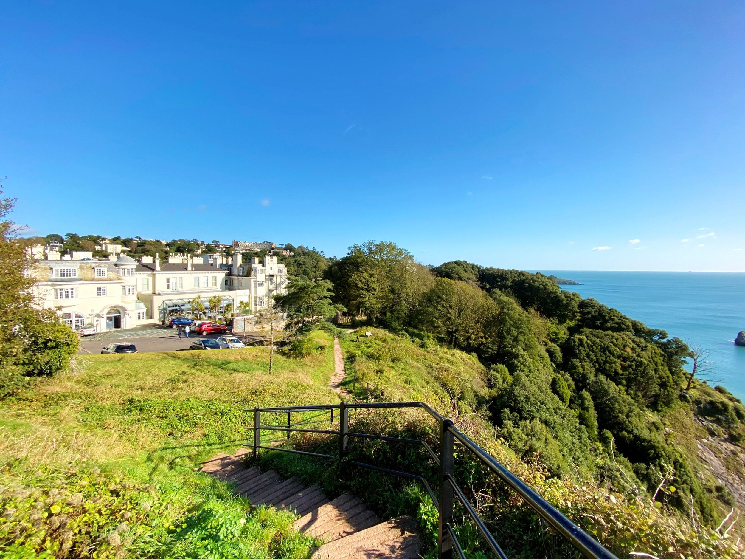 A coastal building with a paved area and a staircase leading down to a path.