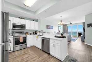 A modern kitchen with white cabinetry, stainless appliances, and a view to the living area. - ☀️Gulf Dunes 516 - Gulf Glimmer | Gulf Front Views | Beach Service☀️ (Fort Walton Beach)