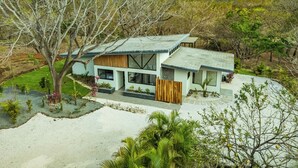 A modern two-story house with a flat roof, large windows, and a stone pathway leading to the entrance. - Casa Ceiba: Lush 3BR Escape Near the Ocean (Paraíso)