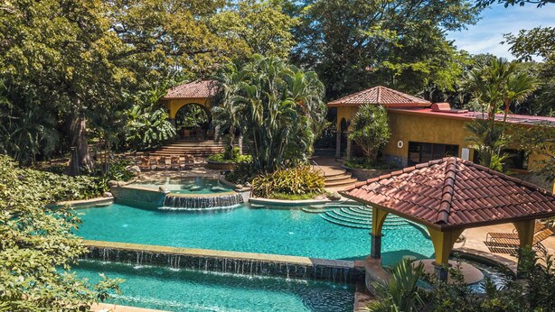 A multi-level swimming pool with a waterfall feature, surrounded by lush greenery and traditional architecture. - Casa Ceiba: Lush 3BR Escape Near the Ocean (Paraíso)