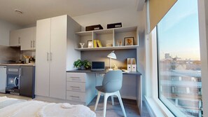 A modern kitchen with grey cabinets, a built-in oven, and a dining area with a white rug and grey chair. - Student Only iQ City (London)