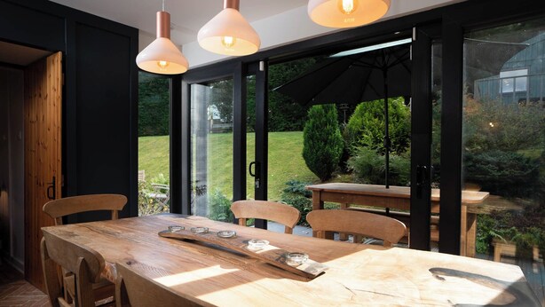 A dining area with a wooden table and chairs, large windows, and hanging pendant lights. - Cosy and stylish, dog and family friendly cottage just south of Aviemore (Dalraddy)