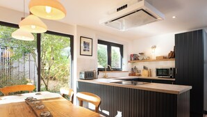 A modern kitchen with a central island, a dining area with wooden furniture, and a large window providing a view of the outdoors. - Cosy and stylish, dog and family friendly cottage just south of Aviemore (Dalraddy)
